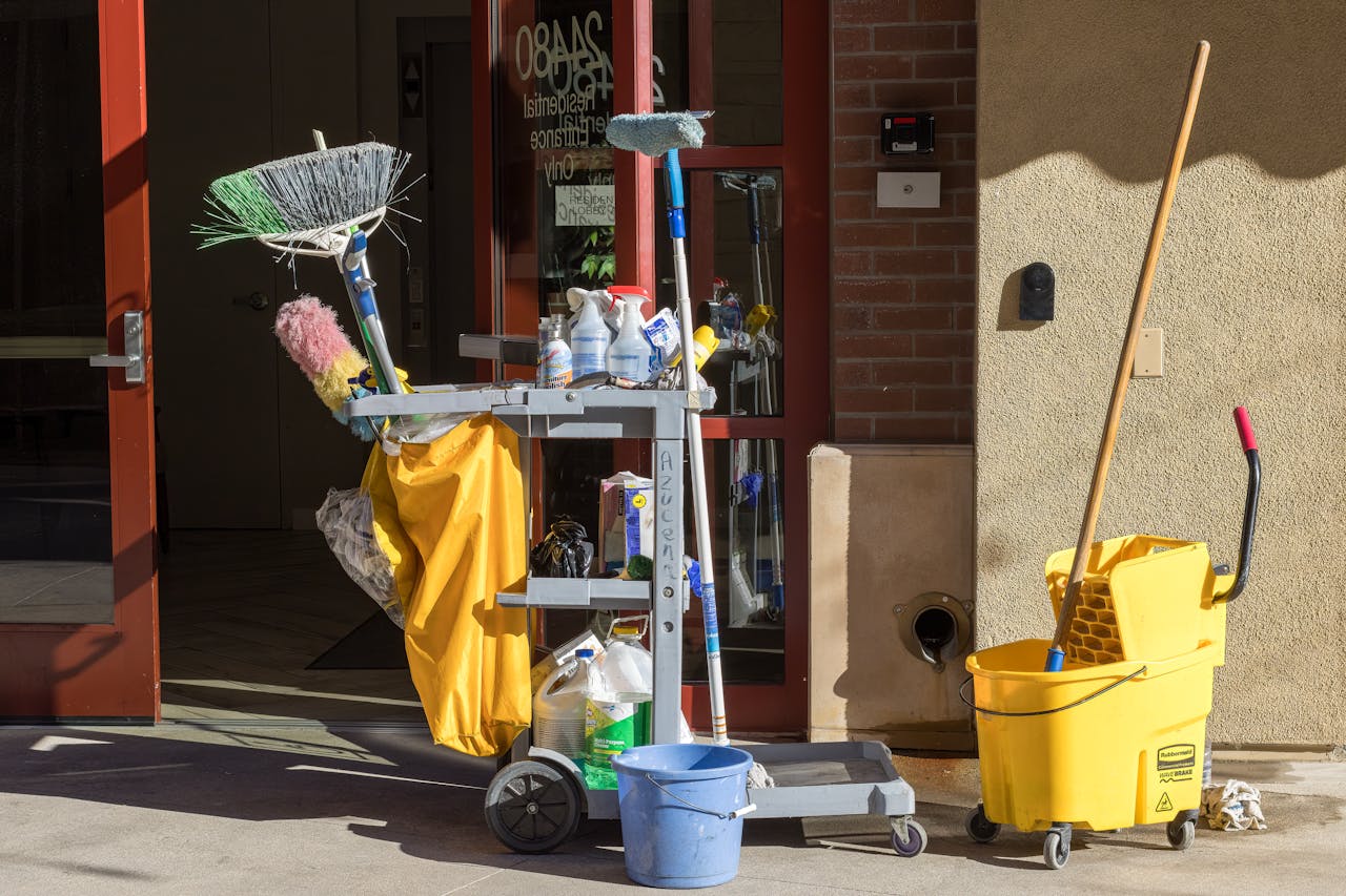 services-04 Cleaning supplies and tools outside a building entrance bathed in sunlight.